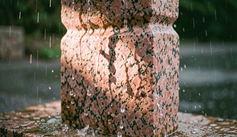 Bloc de granit rose ruisselant après une averse, une trouée de lumière en fait ressortir la couleur