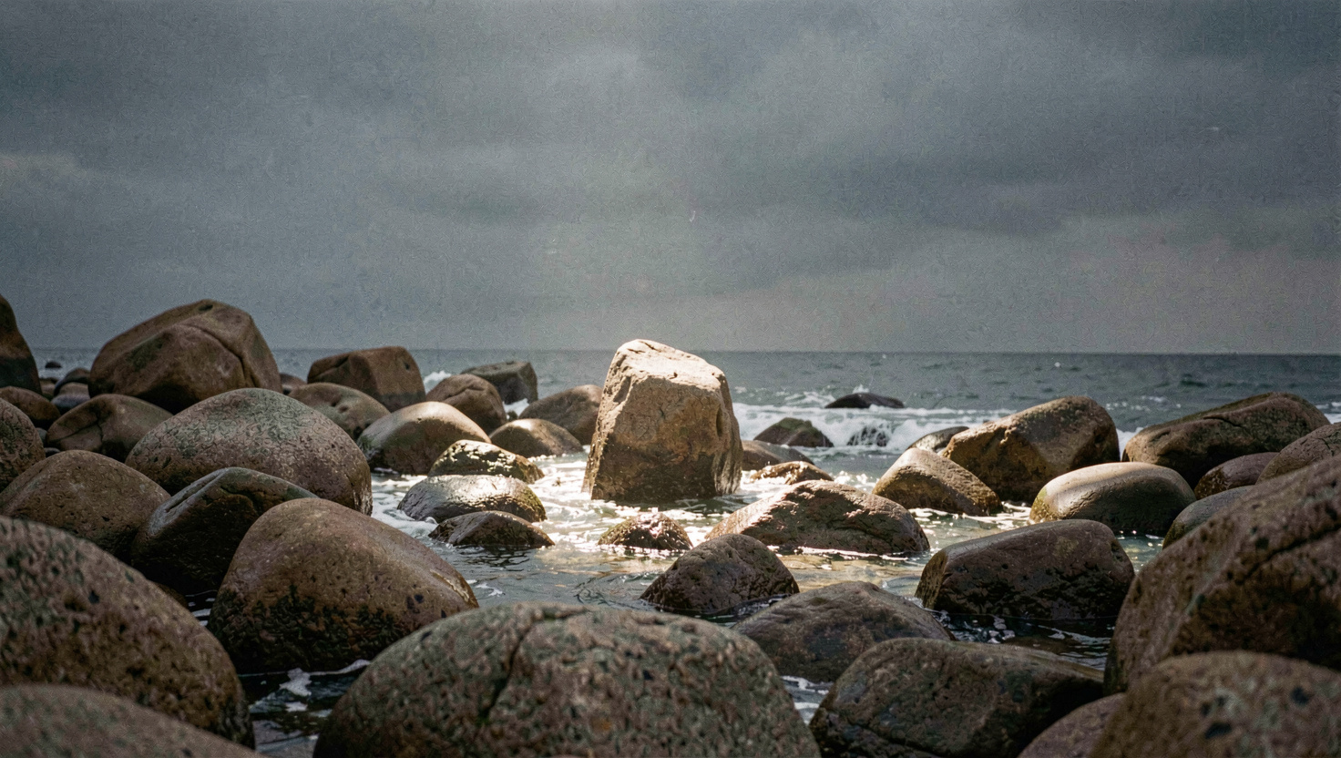Chaos de rochers de granit arrondis au bord de la mer, une trouée de lumière éclaire un seul bloc pendant que le ciel reste sombre