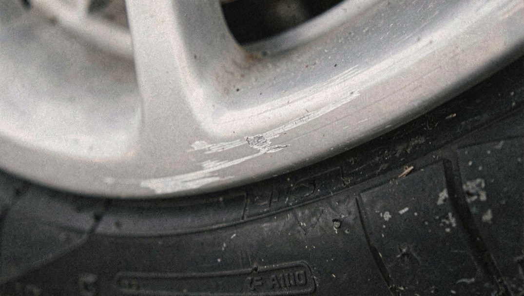 Gros plan sur une jante en aluminium d'une voiture, une éraflure claire sur le bord extérieur de la jante, le pneu noir au-dessous, lumière douce de côté
